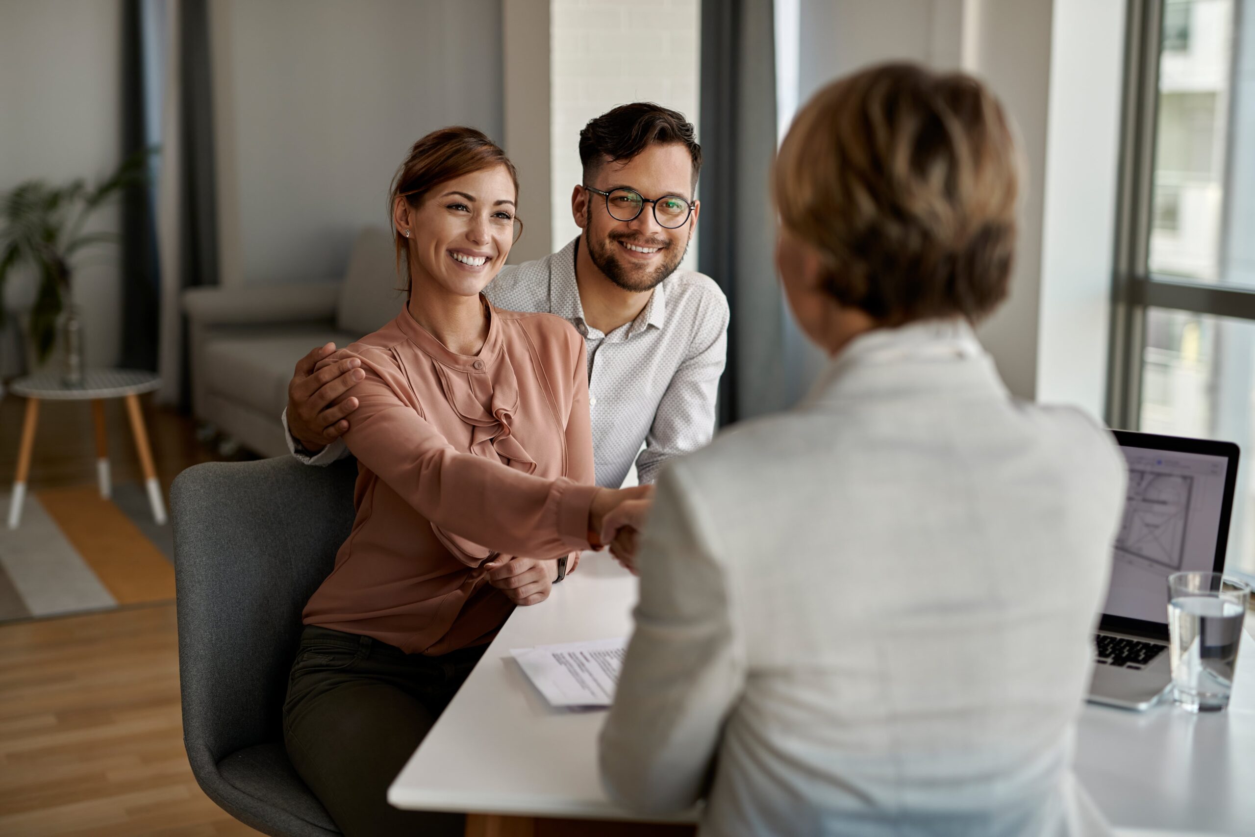 young-happy-couple-shaking-hands-with-insurance-agent-meeting-office-min